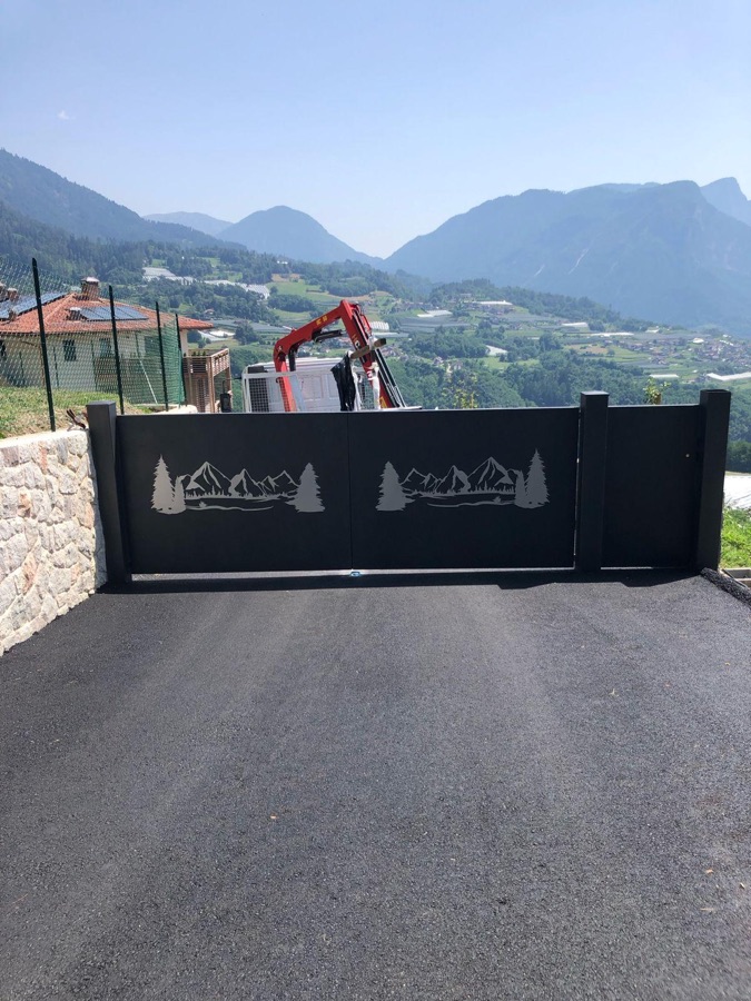 Cancello scorrevole con il profilo delle Dolomiti e dei pini tagliato al laser, a Strigno.