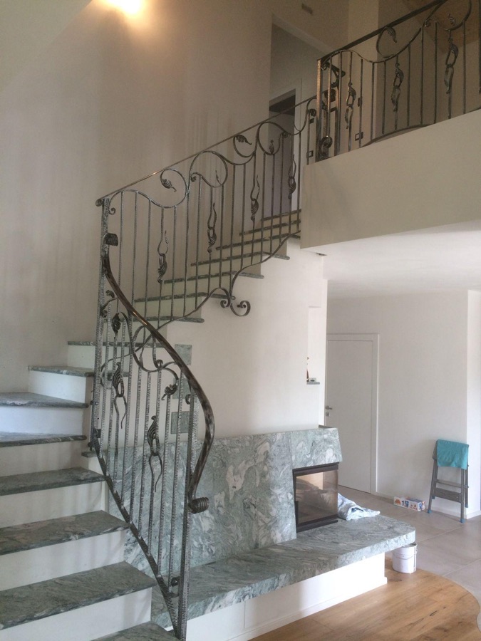 Scala interna con ringhiera in ferro battuto lavorato a mano con volute e foglie, a Terre d’Adige.